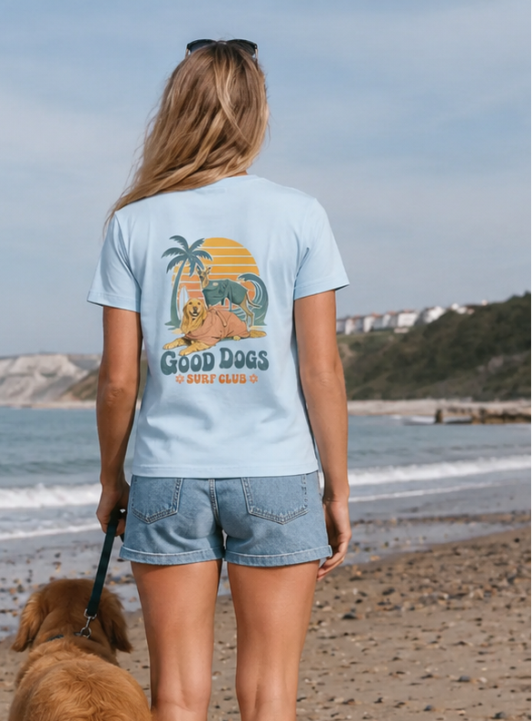 Woman walking a dog on a beach wearing a t-shirt with a graphic design.
