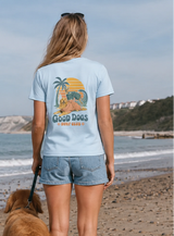 Woman walking a dog on a beach wearing a t-shirt with a graphic design.